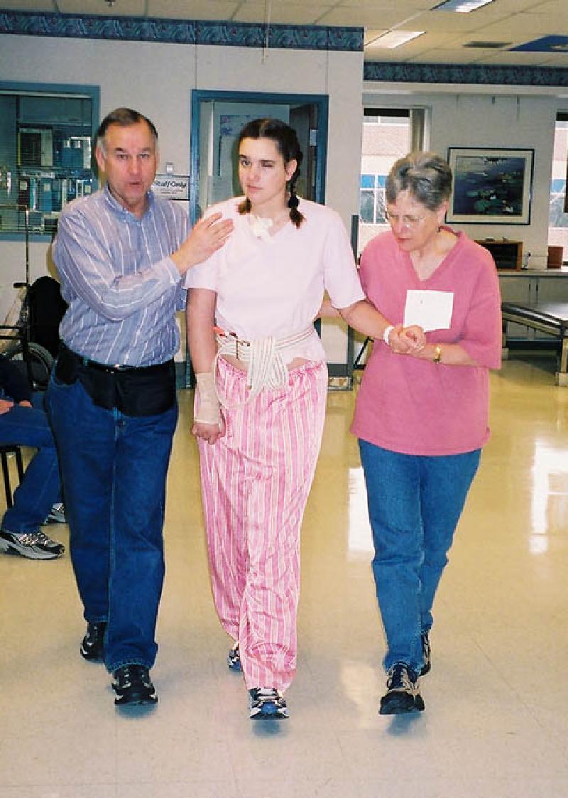 Marla walking with support from Mom and Dad, who are learning the proper techniques for walking with Marla.